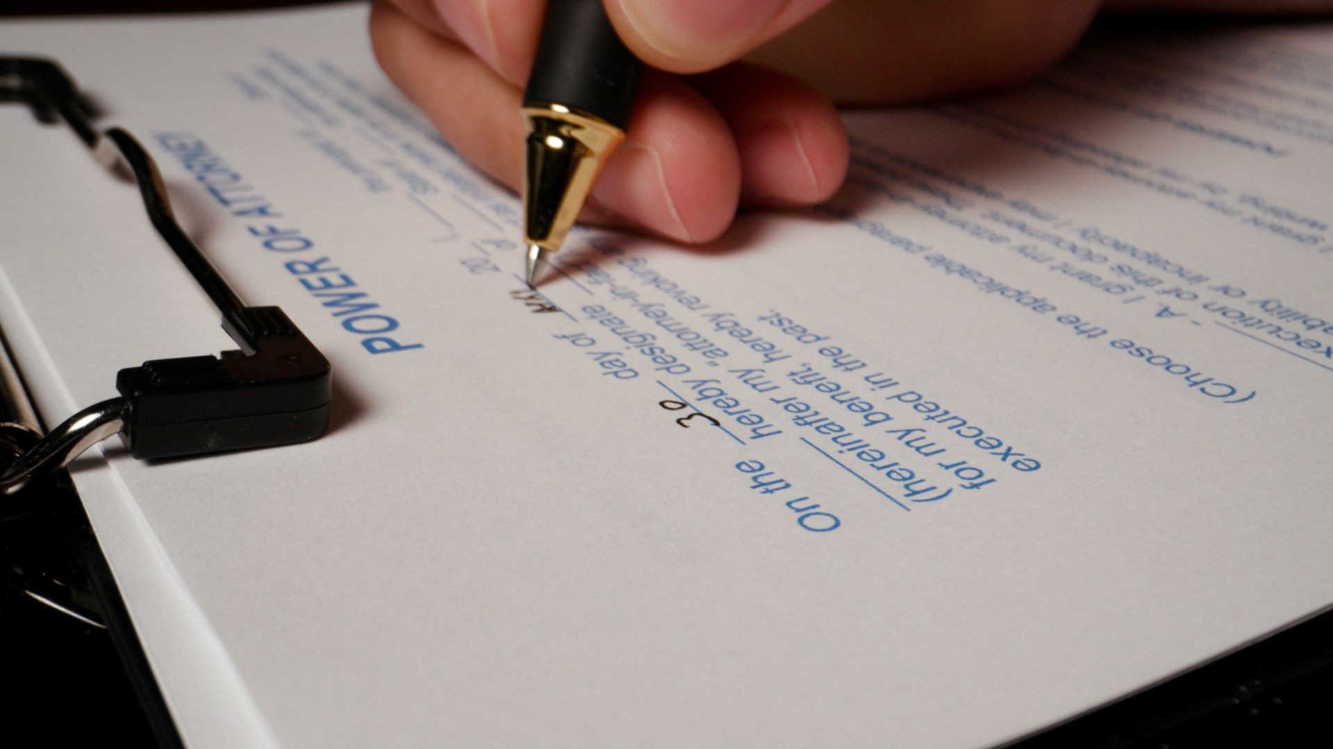 Closeup of man holding a pen to fill out a power of attorney form.